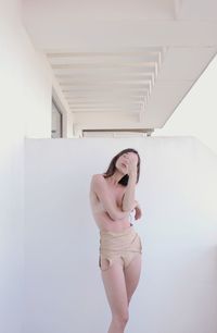 Shirtless young woman standing against wall