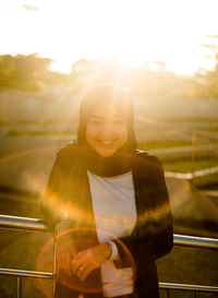 Portrait of smiling young woman standing against bright sun