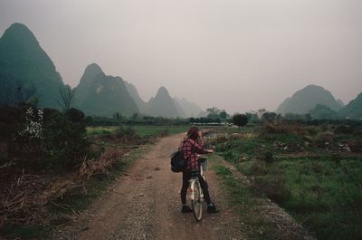 Rear view of young woman with bicycle on dirt road