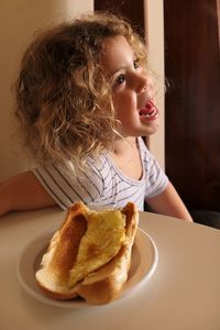 Girl looking away while sitting at table with breakfast