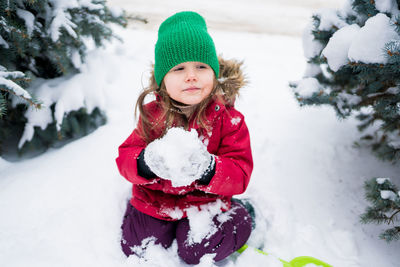 Cute girl holding snow while sitting outdoors