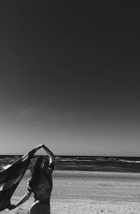 Rear view of young woman holding scarf standing at beach against sky