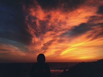 Silhouette woman on beach against orange sky