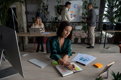 Serious brunette businesswoman wearing green shirt writing notes. open space coworking office