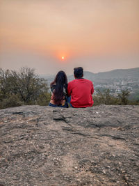 Rear view of woman walking on field against sky during sunset
