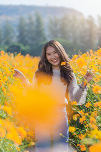 Portrait of woman standing by yellow flowering plants