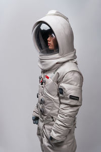 Asian woman in astronaut costume and helmet looking away during space mission against gray background