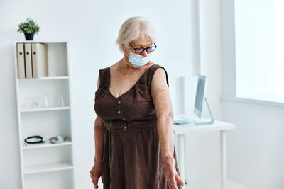 Senior woman wearing mask standing at hospital for vaccination