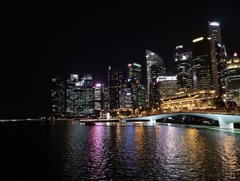 Illuminated buildings by river against sky at night