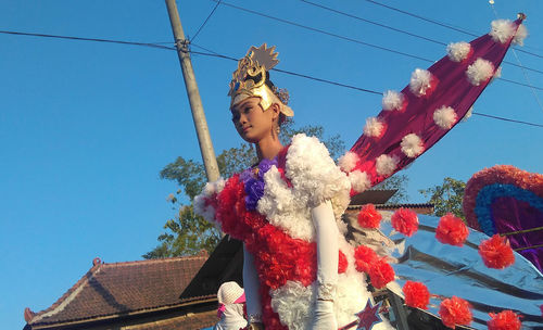 Low angle view of young woman wearing carnival costume while standing against clear blue sky