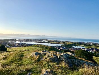 Scenic view of landscape and sea against clear blue sky