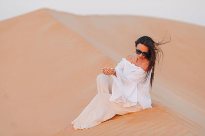 Midsection of woman wearing sunglasses on sand at desert