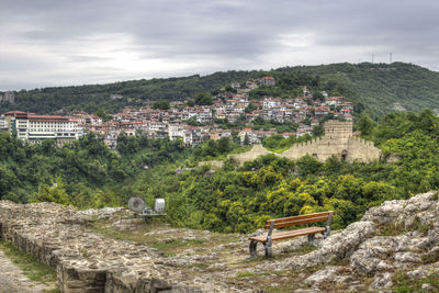 Bench with view of residential district on mountain with bench in foreground against cloudy sky