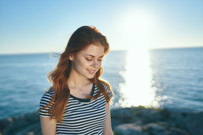 Young woman smiling while standing against sea