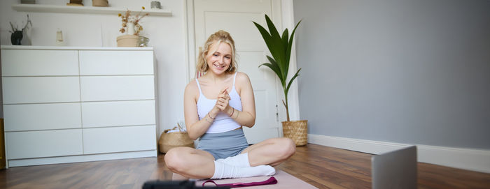 Full length of woman sitting on hardwood floor at home