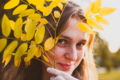 Close-up portrait of young woman holding yellow autumn leaves