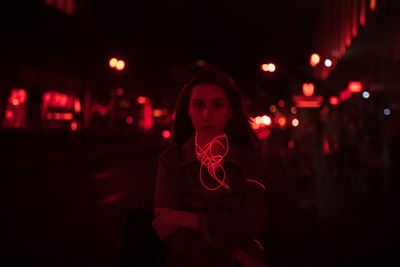 Portrait of young woman standing on road at night