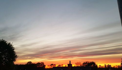 Low angle view of silhouette trees and buildings against sky during sunset