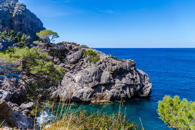 Scenic view of cliff by sea against blue sky
