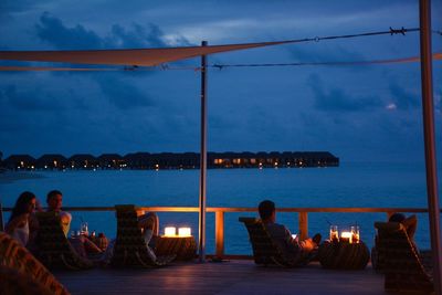 People sitting on table by sea against sky at night