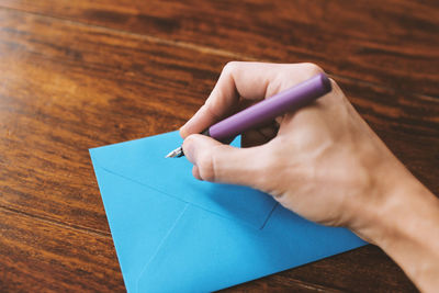 Cropped image of man writing on blue envelope