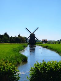 Traditional windmill on landscape against clear blue sky