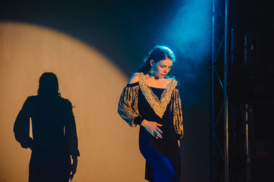 Young woman standing against illuminated wall at night