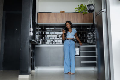 Young black woman working at home with smartphone in the kitchen of apartment. home office.