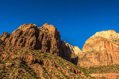 Low angle view of rocky mountains against clear blue sky