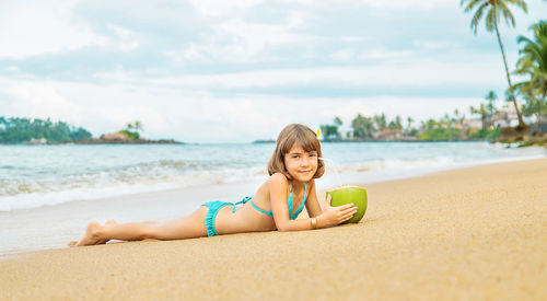 Portrait of smiling girl with coconut lying on beach