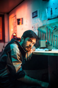 Portrait of serious man sitting at illuminated workshop