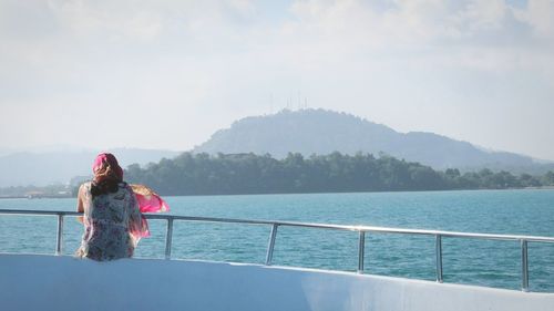 Rear view of woman standing by sea against sky