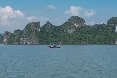 Boat sailing on sea by mountain against sky