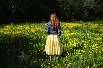 Rear view of a red haired young woman on flower meadow