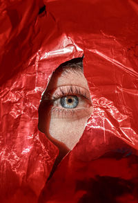 Close-up eye peeking thrrough torn red paper.