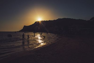 Silhouette people on beach against sky during sunset