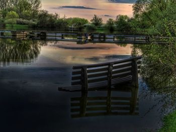 Empty bench by lake against sky