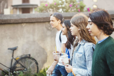 Side view of teenagers holding disposable glasses while walking outdoors