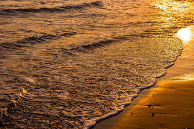 Waves approaching beach sand during golden sunset. saturated image