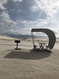 Empty bench on beach against sky