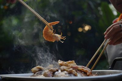 Close-up of hand holding meat on barbecue grill