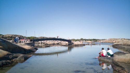 People on bridge over river against clear sky