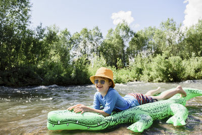 Boy wearing bucket hat lying on inflatable crocodile