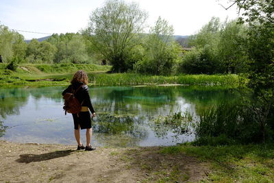 Rear view of woman standing by lake against trees