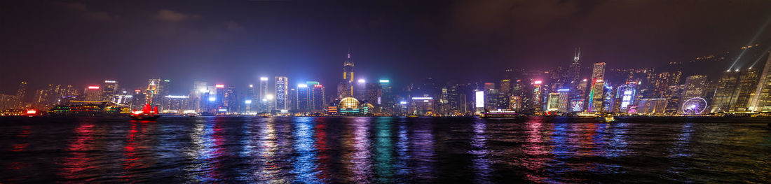 Illuminated buildings by river against sky at night