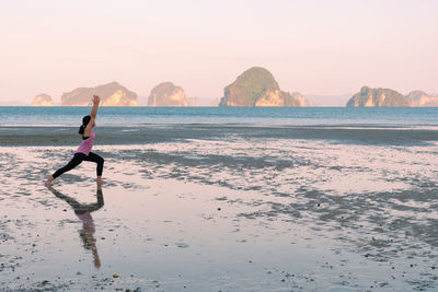 Young asian woman workout by doing yoga on the beach at sunrise