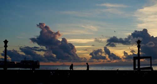 Silhouette people standing by sea against sky during sunset