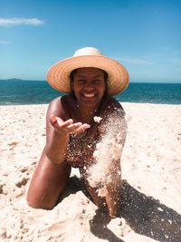 Smiling woman playing with sand while kneeling at beach