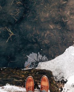 Low section of man standing on cliff by lake in winter