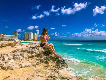 Woman sitting on rocks at beach against sky